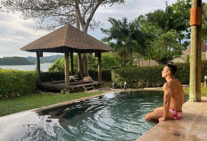 Gay traveler at luxury pool villa, The Naka Island Resort & Spa, Phuket. Man in swimwear enjoys Thailand hotel's private pool and spa.