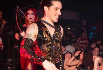 Posh Club Lisbon nightlife scene. Smiling man in a sequin vest, with a drag queen in the background. Gay travel advice in Lisbon, Portugal.