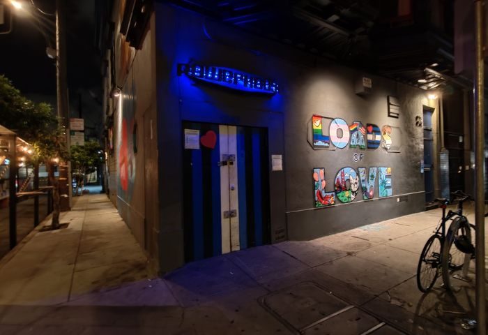 Powerhouse Gay Bar in San Francisco. Night shot of the entrance with Loads of Love graffiti art. Blue-striped door, bike parked nearby.