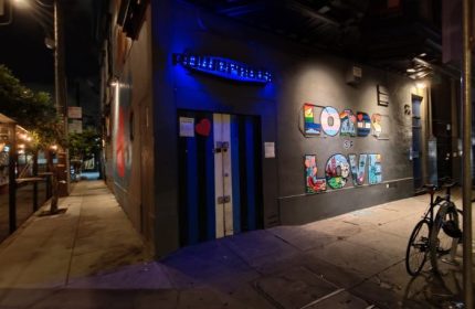 Powerhouse Gay Bar in San Francisco. Night shot of the entrance with Loads of Love graffiti art. Blue-striped door, bike parked nearby.