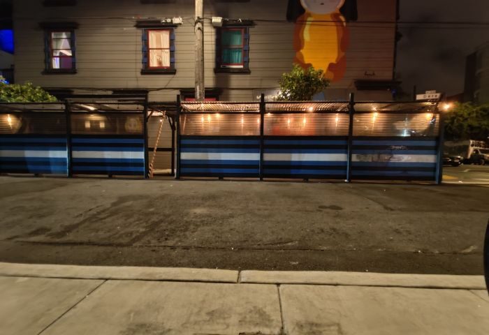 Powerhouse Gay Bar in San Francisco. Outdoor seating area with blue and white striped barriers, lit by string lights. Night scene.
