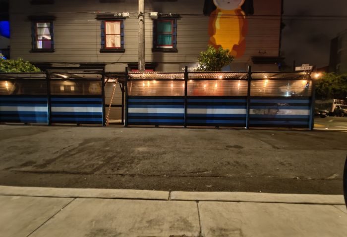 Powerhouse Gay Bar in San Francisco. Outdoor seating area with blue and white striped barriers, lit by string lights. Night scene.