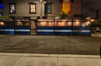 Powerhouse Gay Bar in San Francisco. Outdoor seating area with blue and white striped barriers, lit by string lights. Night scene.