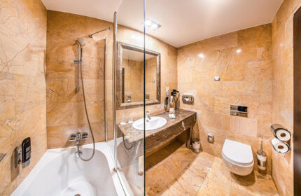 Grandior Hotel Prague bathroom. Marble-tiled bathroom with bathtub, shower, sink, mirror, and toilet. Gay-friendly hotel near metro.