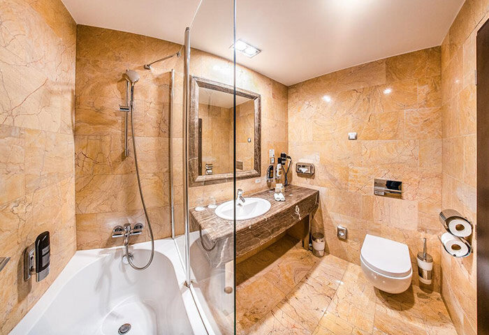 Grandior Hotel Prague bathroom. Marble-tiled bathroom with bathtub, shower, sink, mirror, and toilet. Gay-friendly hotel near metro.