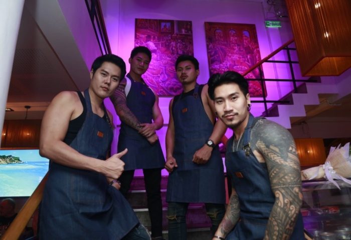 Pride Bar and Restaurant in Bangkok: Four attractive Asian men in aprons pose. Gay bar staff with tattoos and purple lighting.