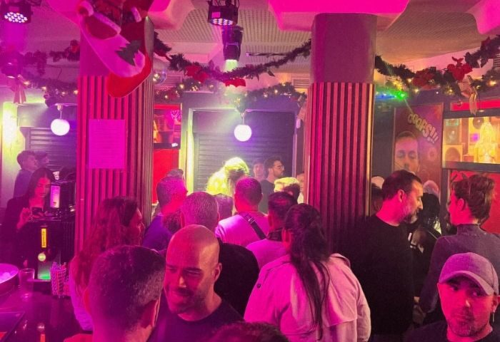 Inside Prima S-Bar, a gay bar in Madrid, featuring a crowd of people, festive decorations, and a lively atmosphere. Nightlife scene.