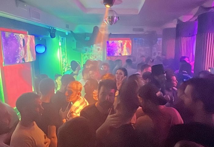 Crowded Prima S-Bar, popular gay bar in Madrid. Disco ball, colorful lights, and screens create a vibrant atmosphere for gay nightlife.