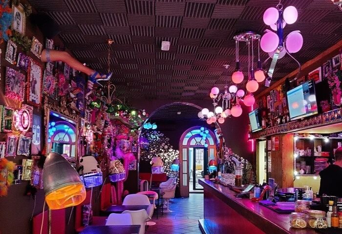 Interior of Priscilla Cafe Gay Bar in Barcelona. Eclectic decor, pink lighting, and vintage hair dryers. Gay travel destination.