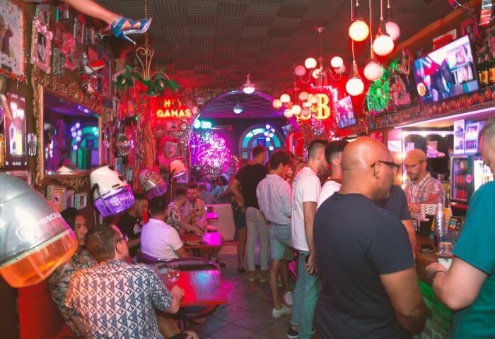 Interior of Priscilla Cafe Gay Bar in Barcelona. Patrons at bar, neon lights, quirky decor. Gay men travel advice.