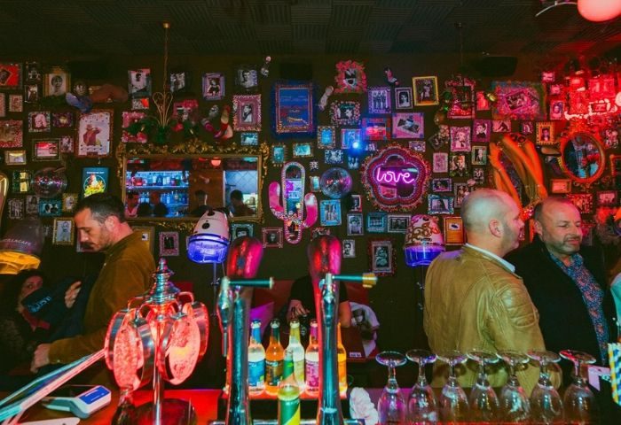 Priscilla Cafe Gay Bar in Barcelona: Interior view with men at the bar, eclectic decor, and vibrant atmosphere. Gay travel advice.
