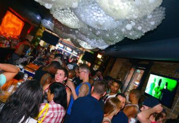 Progress Bar Chicago gay party nights. Crowded gay bar scene with diverse crowd, bar, and unique ceiling decor. Nightlife for gay men travel.
