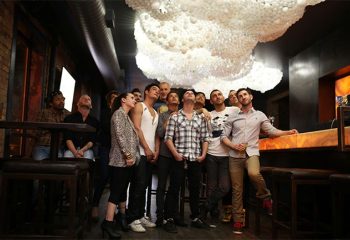 Gay party nights in Chicago: Group of people looking up at a unique cloud-like light fixture in a bar. Nightlife scene.