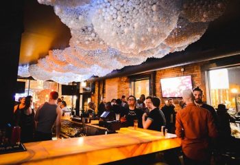 Gay party nights in Chicago: Interior view of a crowded gay bar. Decorative ceiling, bar with patrons, and TVs in the background.