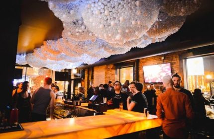 Gay party nights in Chicago: Interior view of a crowded gay bar. Decorative ceiling, bar with patrons, and TVs in the background.