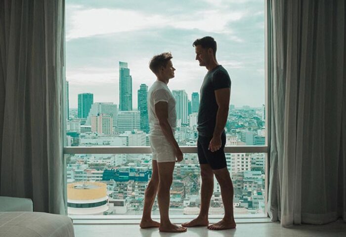 Gay couple at Pullman Bangkok Hotel G. Two men stand in front of a window with Bangkok skyline view. LGBT travel advice.
