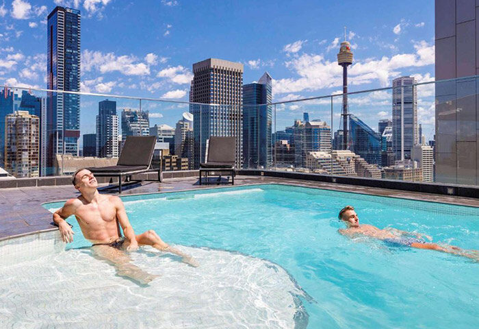 Gay honeymoon at Pullman Sydney Hyde Park. Two men relax in the rooftop pool with city skyline views. Number 1 gay hotel.