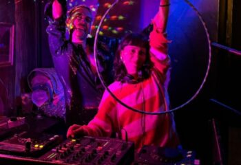 Nightlife at Purex, Lisbon's gay club: a DJ spins tunes under disco lights. A man in sequins dances, adding to the vibrant atmosphere.