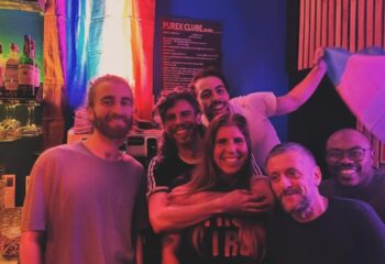 Group of smiling people at Purex Clube, Lisbon. Rainbow flag visible. Gay travel advice, nightlife, and LGBTQ+ friendly bar.