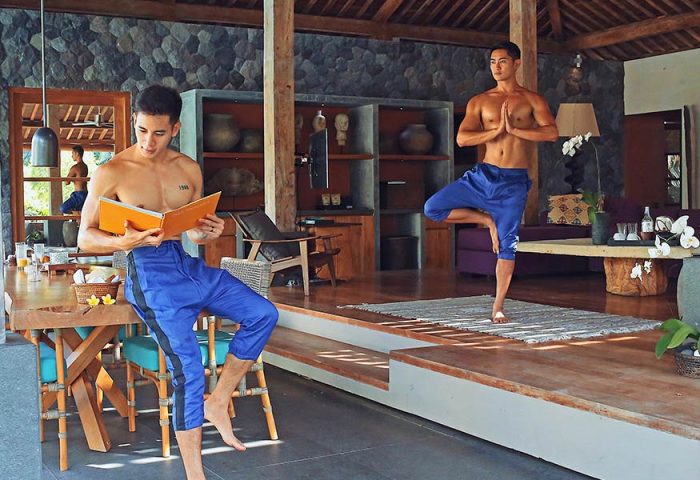 Gay travel: Two shirtless men at Purist Villas, Ubud, Bali. One reads, the other does yoga. Luxury gay-friendly resort.