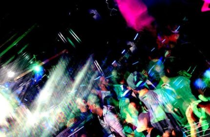 QClub Milan gay party scene. Blurry image of a crowded dance floor with colorful lights. Gay nightlife in Milan, Italy. Men dancing.