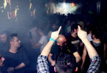 QClub Milan: Gay men partying in a dark, smoky nightclub with lights and music. People are dancing and having fun at this gay venue.