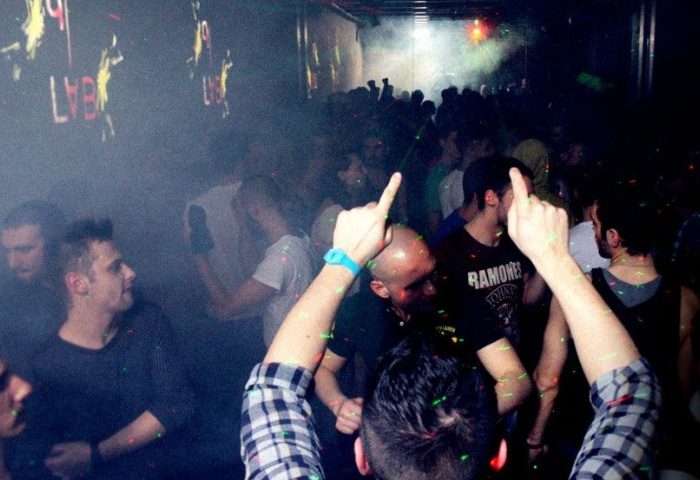 QClub Milan: Gay men partying in a dark, smoky nightclub with lights and music. People are dancing and having fun at this gay venue.