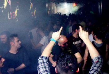 QClub Milan: Gay men partying in a dark, smoky nightclub with lights and music. People are dancing and having fun at this gay venue.