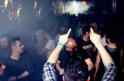 QClub Milan: Gay men partying in a dark, smoky nightclub with lights and music. People are dancing and having fun at this gay venue.