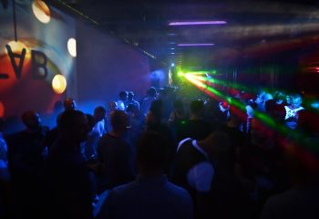 Q Club Milan: Gay men dancing in a crowded nightclub with colorful laser lights and a vibrant atmosphere. Milan's gay nightlife scene.
