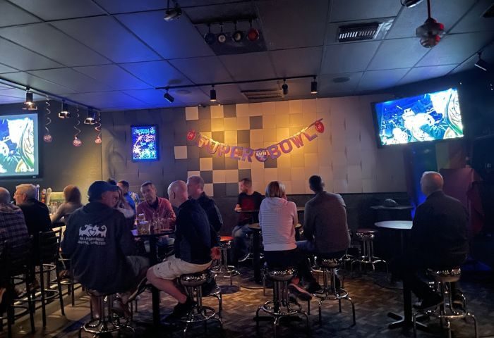 QUADZ Bar scene. Gay bar patrons watch Super Bowl on TVs. Super Bowl banner on wall. Gay men travel advice.