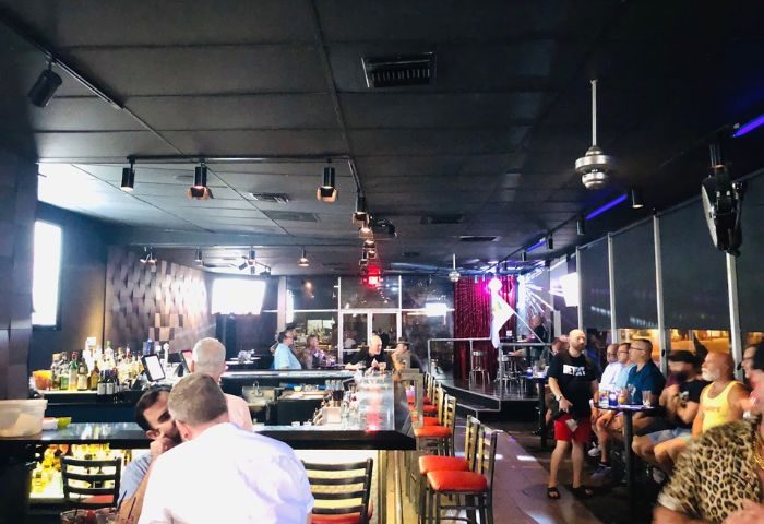 QUADZ Experience: Interior of a gay bar, with men socializing at the bar and tables. Stage with rainbow flag. Gay travel advice.