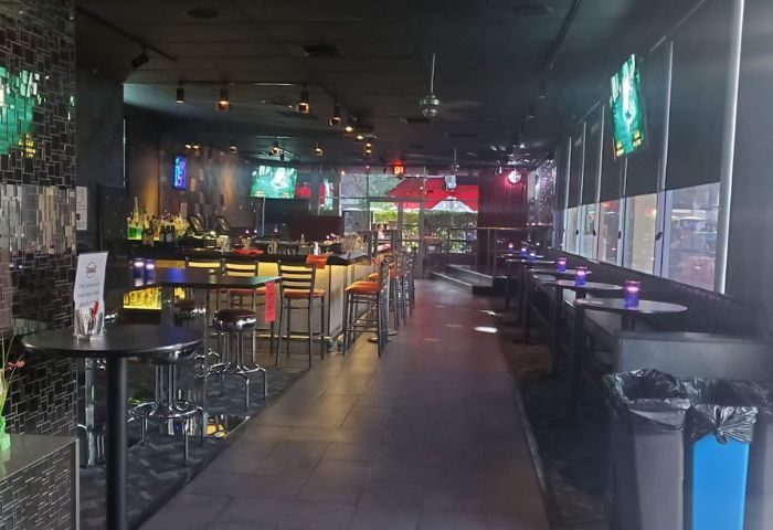 QUADZ: Interior of a gay bar. Bar stools line the counter, tables with chairs, TVs, and a dark ambiance. Nightlife for gay men travel.