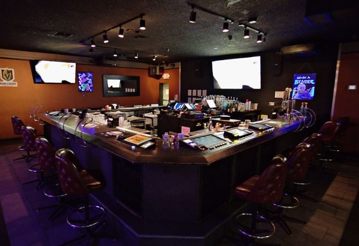 Interior of Quadz Video Bar in Las Vegas, a gay bar featuring a long bar with stools, TVs, and a wide selection of drinks. Nightlife.