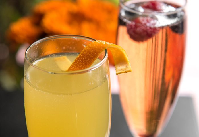 Queen Bee cocktail. Two champagne flutes, one yellow with orange peel, one pink with berries. Gay men travel advice.