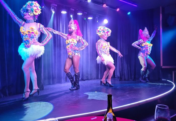 Queenz Cabaret show at a gay bar in Sitges. Four drag queens on stage in colorful costumes with flower headpieces, performing for the audience.
