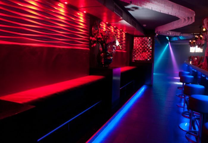 Queenz Music Bar, a gay club in Sitges. Red and blue neon lights illuminate the bar's interior, creating a vibrant, energetic atmosphere.