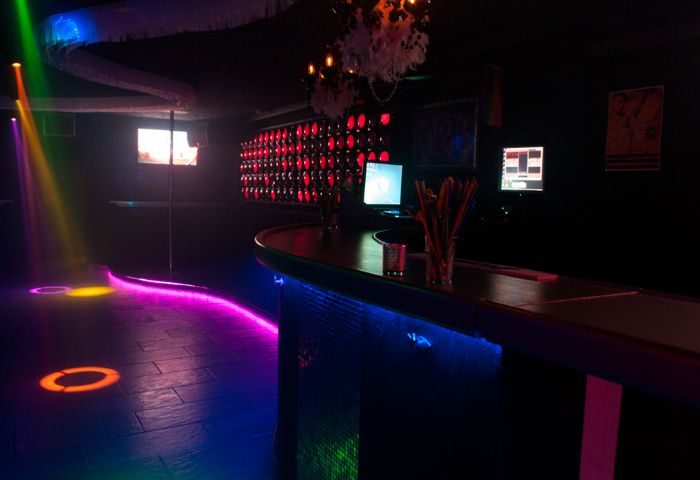 Queenz Music Bar, a vibrant gay club in Sitges. Features a dance floor with colorful lights and a bar with a modern design. Nightlife scene.
