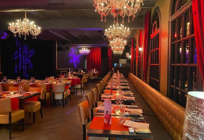 Queenz Music Bar, a gay club in Sitges. Elegant dining area with chandeliers, red accents, and tables set for a meal. Nightlife for gay men.