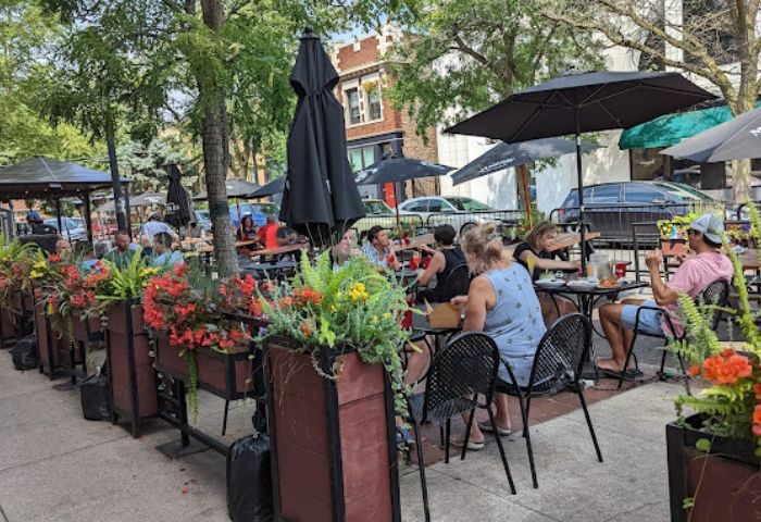 Outdoor seating at REPLAY Andersonville, a gay bar with food in Chicago. People are enjoying drinks under umbrellas on a sunny day.