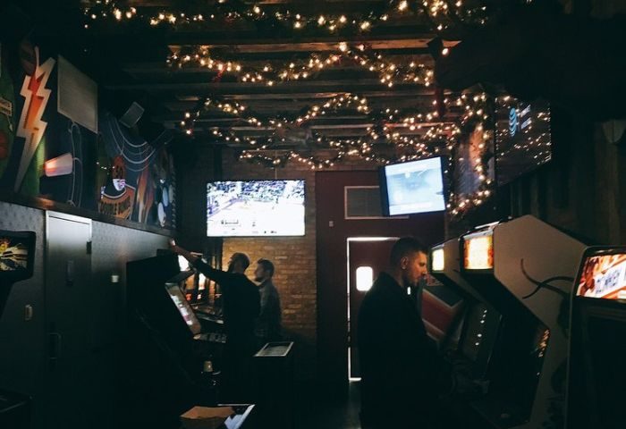Inside Replay Andersonville, a gay bar in Chicago with food. Men play arcade games under string lights and TVs showing sports. Fun gay travel spot.