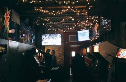 Inside Replay Andersonville, a gay bar in Chicago with food. Men play arcade games under string lights and TVs showing sports. Fun gay travel spot.
