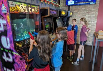 Kids play in Andersonville's Replay gay bar with food in Chicago. Arcade games line brick wall. A fun, family-friendly gay bar experience.