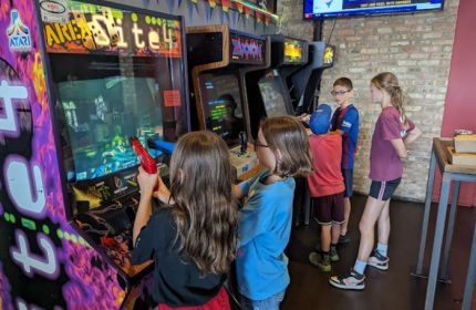 Kids play in Andersonville's Replay gay bar with food in Chicago. Arcade games line brick wall. A fun, family-friendly gay bar experience.