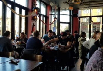 Interior of Replay Andersonville, a gay bar with food in Chicago. People are seated at tables, enjoying food and drinks.