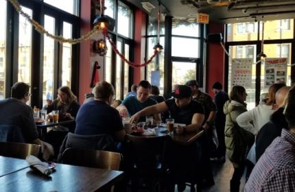 Interior of Replay Andersonville, a gay bar with food in Chicago. People are seated at tables, enjoying food and drinks.