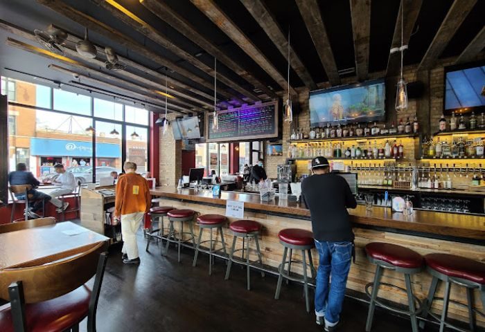 Interior of Replay Andersonville, a gay bar with food in Chicago. Bar with stools, TVs, bottles, and people. Gay travel.