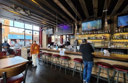 Interior of Replay Andersonville, a gay bar with food in Chicago. Bar with stools, TVs, bottles, and people. Gay travel.