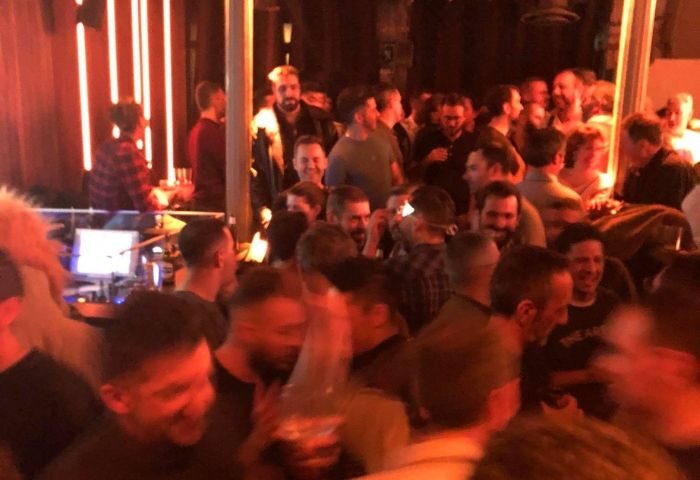 Crowded gay bar in Madrid. Men gather, illuminated by warm light. Travel advice for gay men in Spain. Rick's gay bar nightlife.