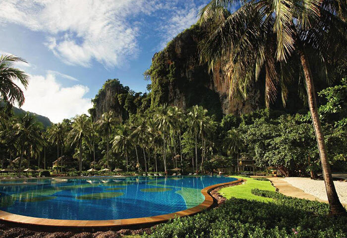 Rayavadee Hotel, a popular gay hotel in Krabi, Thailand. Railay Beachfront view with pool, palm trees, and limestone cliffs.